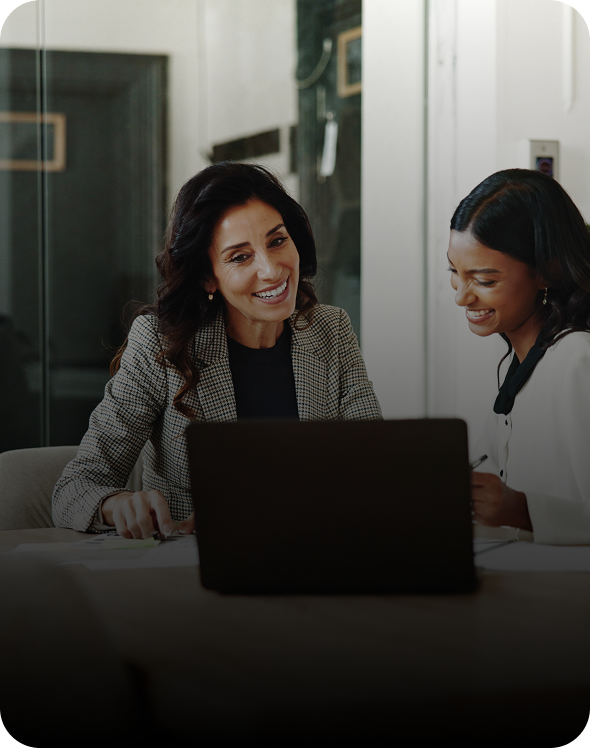Two women smiling while working on laptop.